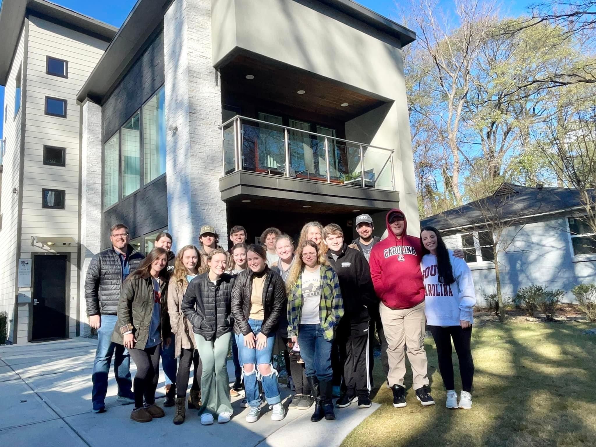 Young adults pose in front of a house on a trip